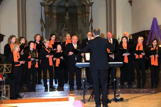 Chor mit orangefarbenen Schals und Dirigent beim Adventskonzert