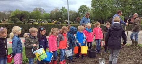 Kinder mit Eimern in einer Reihe am Acker, dahinter Helfer beim Pflanzen