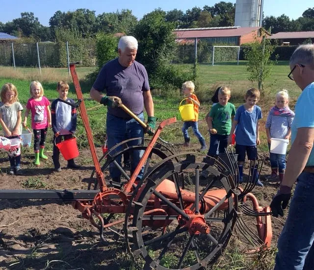 Ein Helfer erklärt den Kindern eine alte Kartoffelrodemaschine