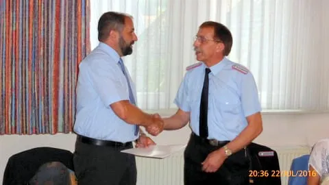 Handschlag zwischen einem Mann im Hemd und einem Feuerwehrmann in Uniform, dazwischen eine Urkunde