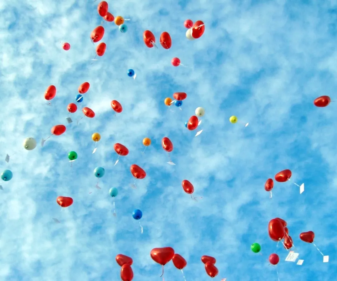 Zahlreiche Luftballons mit Karten steigen in den blauen Himmel