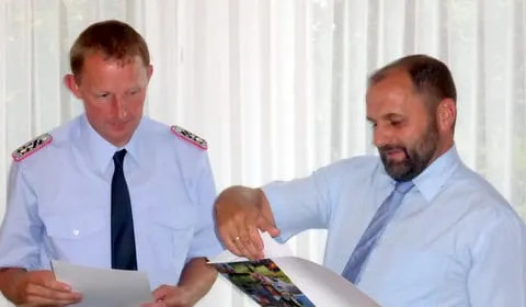 Ein Feuerwehrmann in Uniform und ein Mann im Hemd sehen gemeinsam Unterlagen durch
