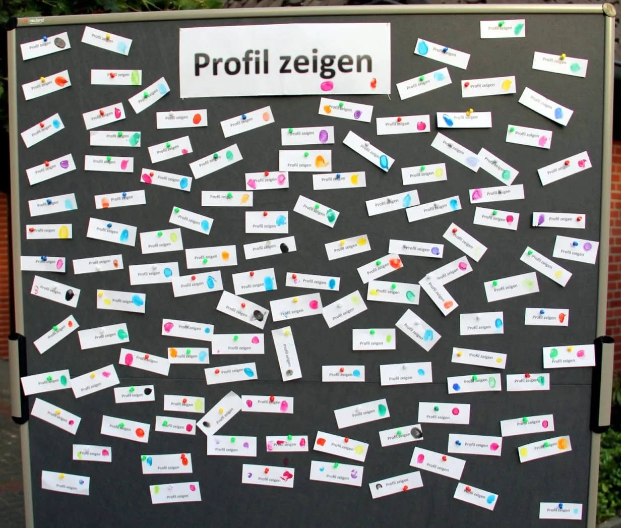 Stellwand mit der Aufschrift „Profil zeigen“, darauf viele Zettel mit bunten Fingerabdrücken