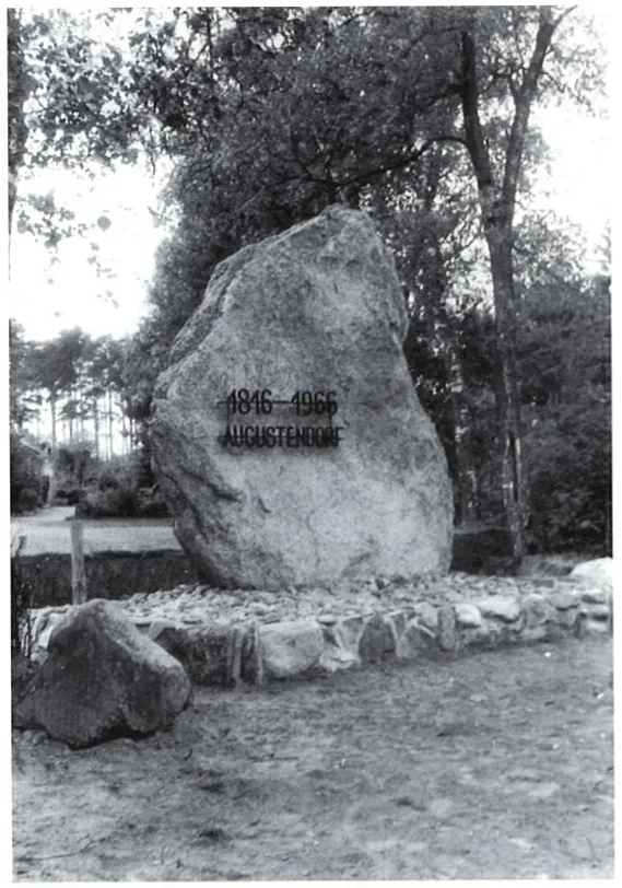 Der Grieser Stein auf seinem Sockel mit der Inschrift „1816–1966 Augustendorf“, dahinter Bäume.