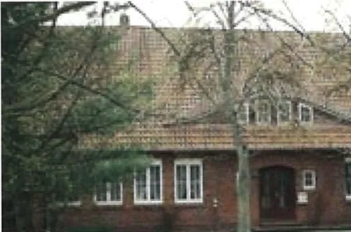 Das Schulhaus von 1911: Backsteinbau mit Satteldach, davor Bäume.