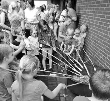 Kinder halten ihr Stockbrot über die Feuerstelle an der Klinkerwand