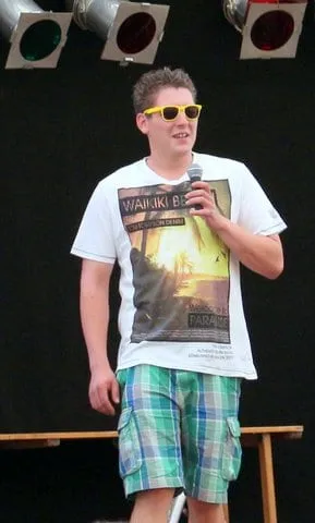 Junger Mann mit Sonnenbrille am Mikrofon auf der Bühne