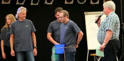 Mannschaft mit einem Eimer auf der Bühne, rechts der Moderator