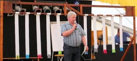 Moderator mit Mikrofon vor der Spielwand auf der Bühne