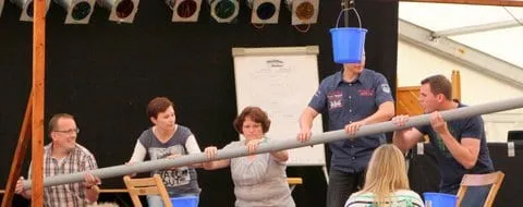 Spielrunde balanciert gemeinsam eine Stange, an der ein Eimer hängt