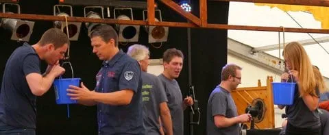 Teilnehmer trinken beim Bühnenspiel aus blauen Eimern