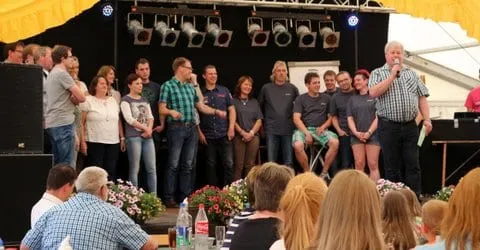 Alle Mitwirkenden auf der Bühne, davor das Publikum an den Tischen
