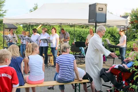 Gemeinde auf Bierbänken, davor der Geistliche, dahinter die Musikgruppe unter dem Pavillon