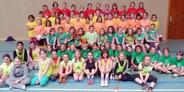 Große Gruppe Grundschulkinder in bunten Mannschaftstrikots in der Sporthalle